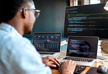 A young man is working on 3 computer screens. A young man is working on 3 computer screens.